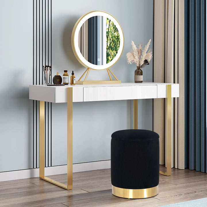 Round velvet storage ottoman with gold base, padded footrest.